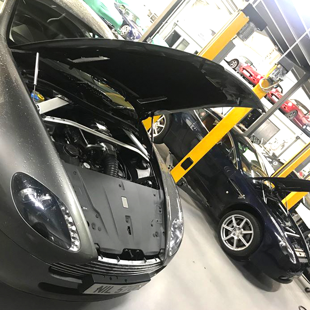 grey and dark blue aston martin cars in topcats racing workshop with bonnets open
