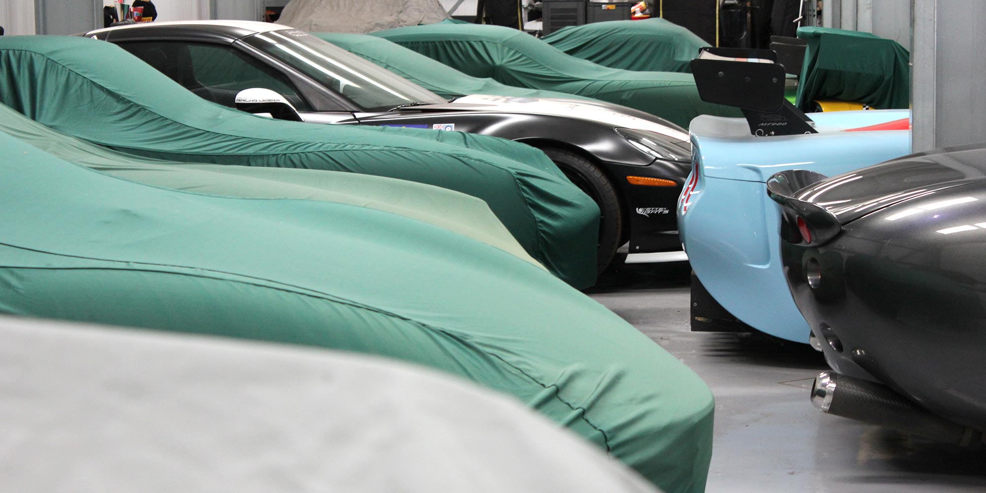 panoramic image of vehicles housed at topcats racing workshop safely stored with car covers
