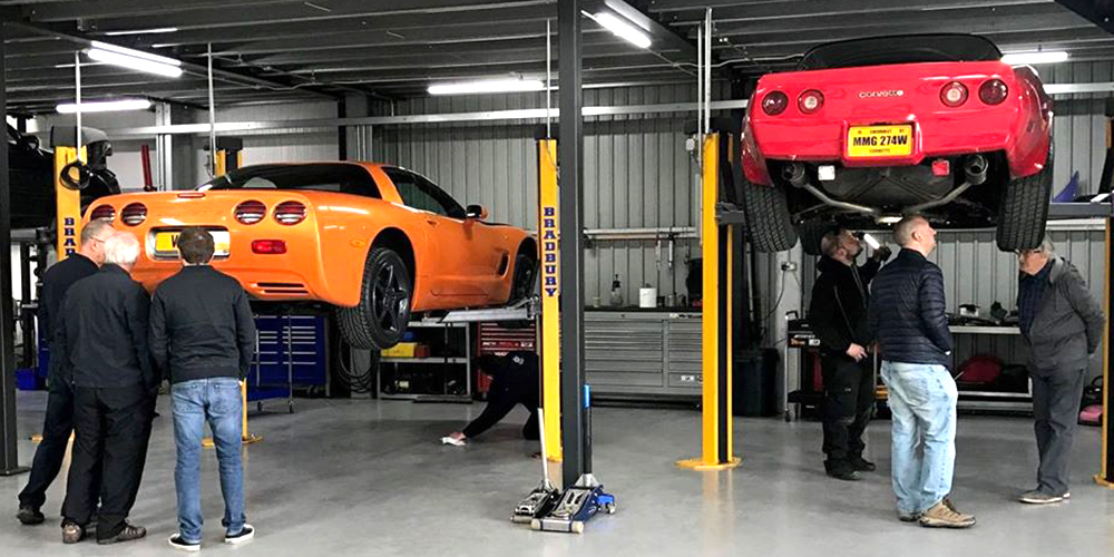 orange chevrolet corvette c6 and red corvette on ramp whilst topcats racing team discuss upgrades